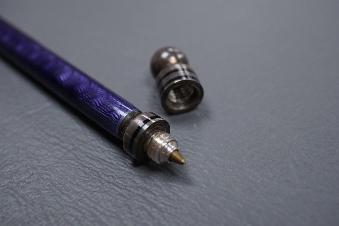 A silver and purple guilloche enamel pen, with ringed black enamel and globe terminals, one unscrews to reveal the pen tip, hallmarks beneath the enamel, possibly London, 1979, 13.9cm.